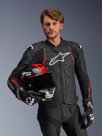 Giacca in pelle Alpinestars Dusk Airflow, nera con accenti Rosso Fluo, indossata da un modello che tiene un casco da moto rosso e nero, con pelle traforata per la massima ventilazione e logo Alpinestars bianco, abbigliamento sportivo da moto