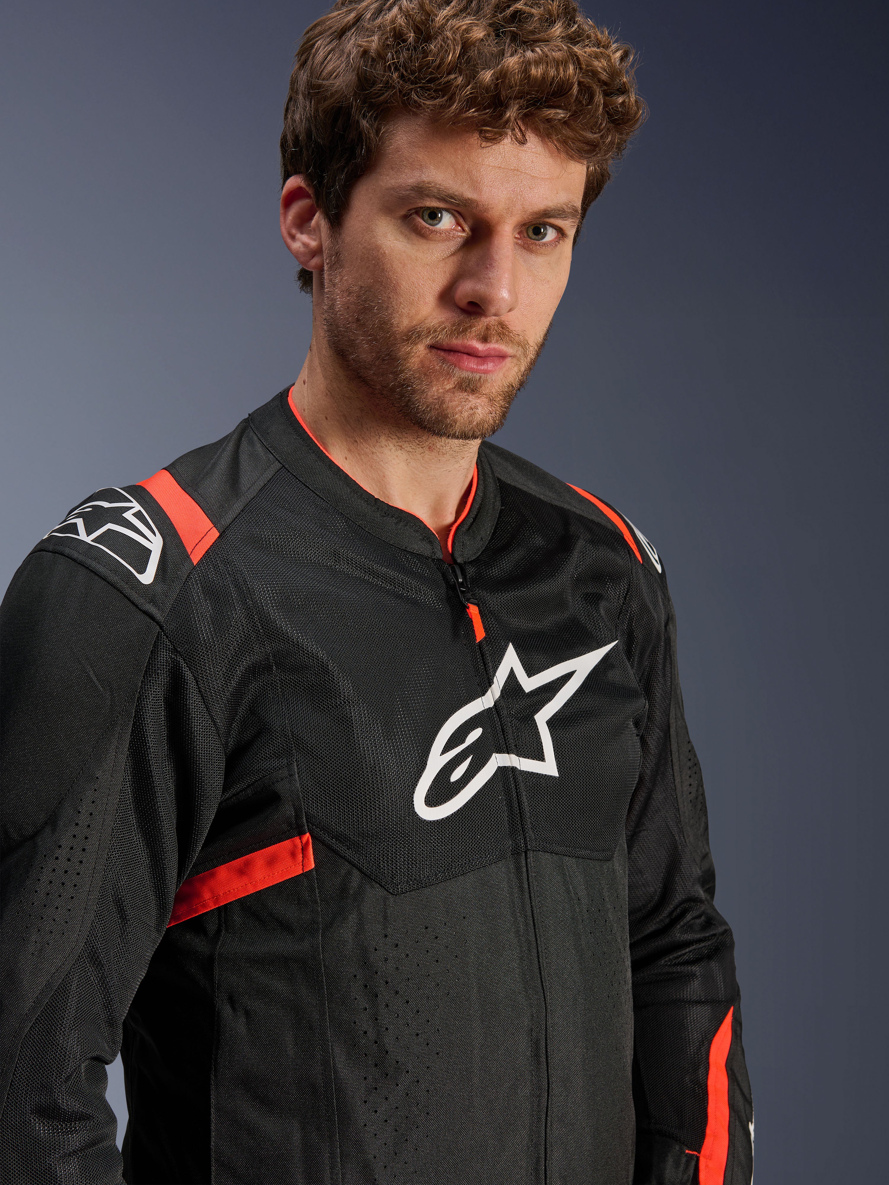 Giacca Alpinestars T-Sps Air V2, nero con accenti rosso fluo, giacca da moto in tessuto mesh, indossata da un modello, con logo Alpinestars bianco sul petto e sulle spalle, pannelli in mesh traspirante, stile urban sportivo