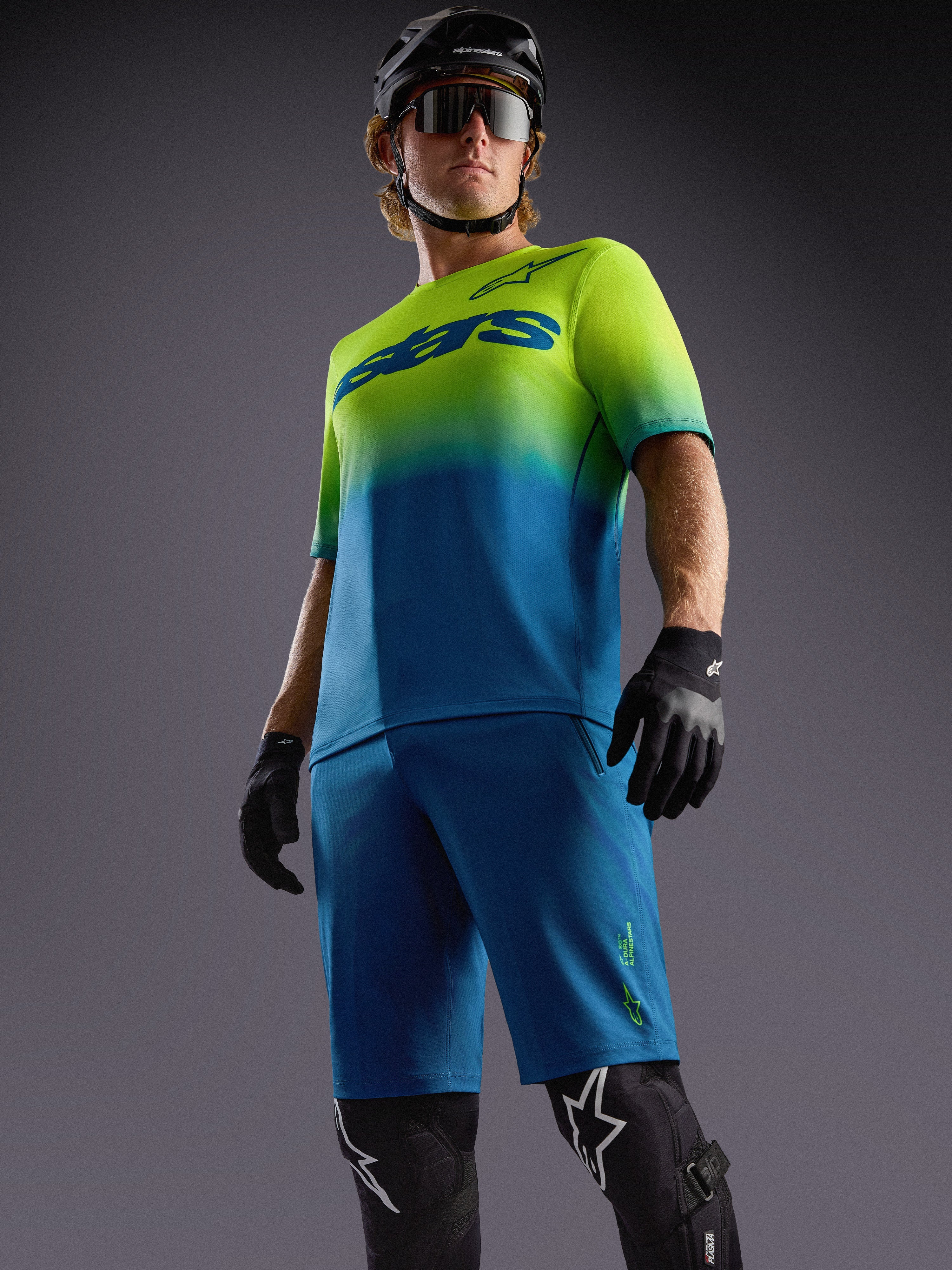 Maglia MTB A-Dura ASTARS 2.0 con sfumatura blu e giallo fluo, maniche corte, pantaloncini e protezioni coordinate.