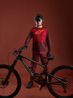 Maglia Alpinestars A-Dura Elite 2.0 bordeaux a maniche lunghe, logo giallo e pannello rosso, con mountain bike.