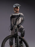 Alpinestars A-Dura Race, maglia grigia a maniche lunghe su rider MTB, dettagli neri e abbigliamento tecnico professionale.