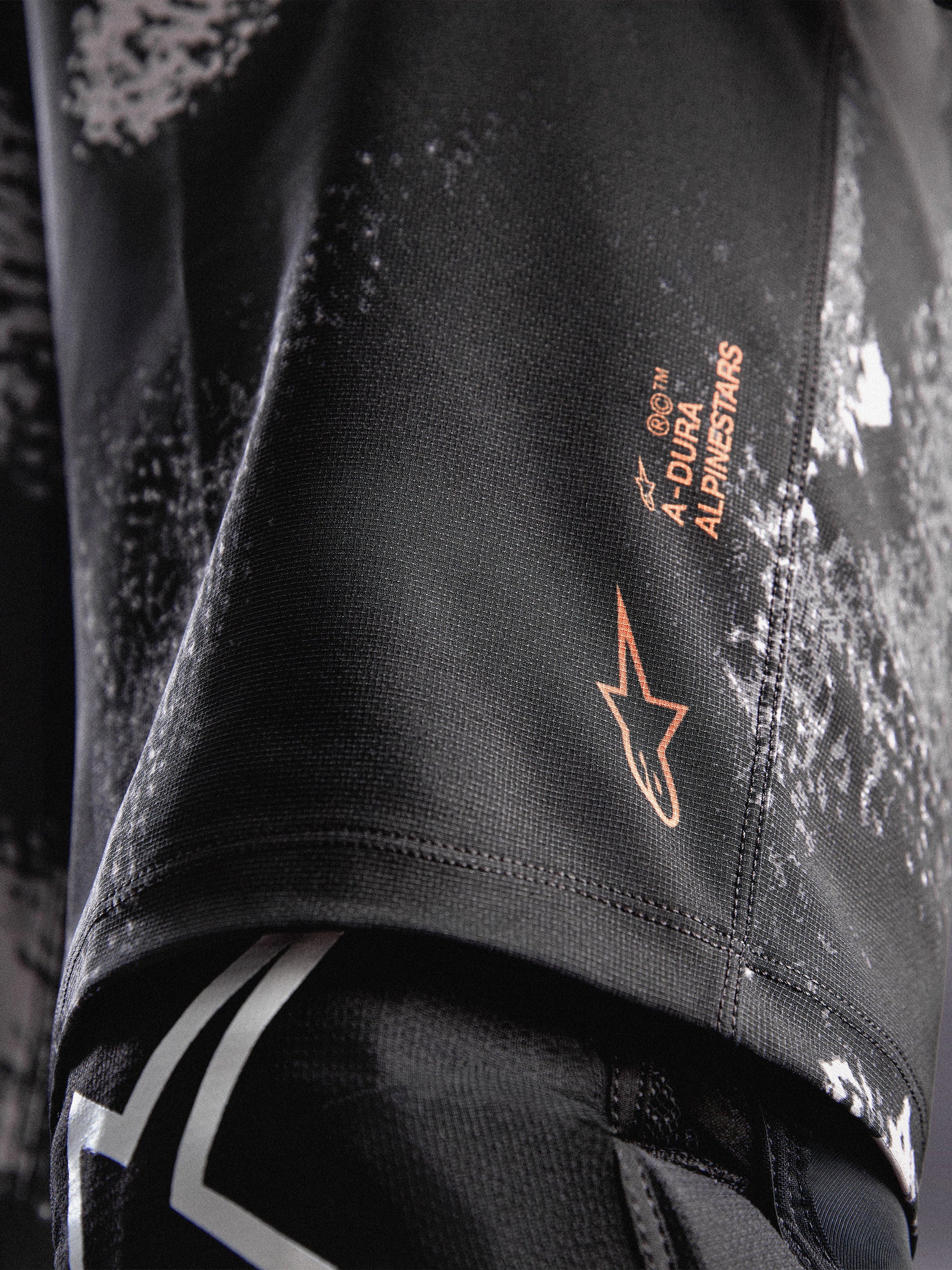 Pantaloncini A-Dura Ride Black Camo, dettaglio logo Alpinestars arancione su tessuto tecnico elasticizzato per MTB.