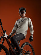 Maglia Alpinestars A-Dura Ride Sand Camo a maniche lunghe con logo sul petto, indossata da un rider su mountain bike.