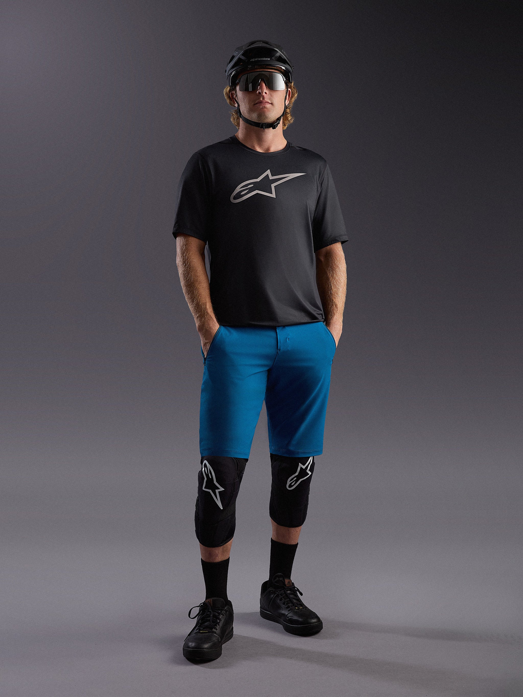 Maglia Alpinestars A-Dura Ride SS nera e pantaloncini blu, outfit completo da MTB con casco e protezioni.