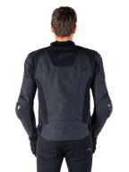 Vista posteriore di un pilota che indossa la giacca in pelle Alpinestars Missile V3 in nero, caratterizzata da una struttura in pelle pregiata con inserti tecnici elasticizzati, logo Alpinestars in rilievo sulla parte bassa della schiena e branding discreto sulla parte superiore, abbinata a pantaloni neri per un look sportivo da corsa coordinato.