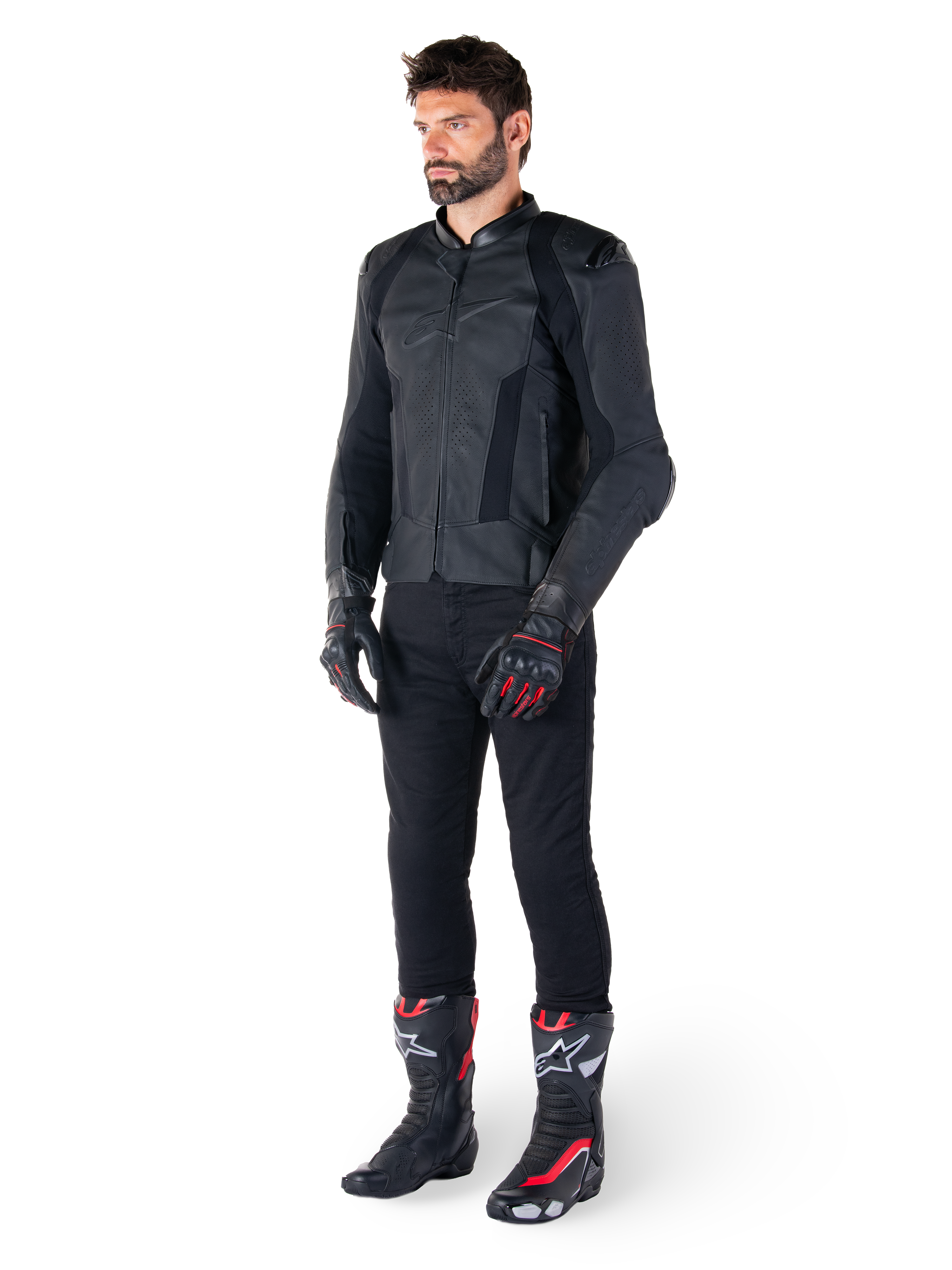 Giacca in pelle Alpinestars Missile V3, nero, indossata da un pilota con pantaloni neri e guanti e stivali da corsa neri e rossi, con pannelli in pelle traforata e branding monocromatico, estetica racing professionale