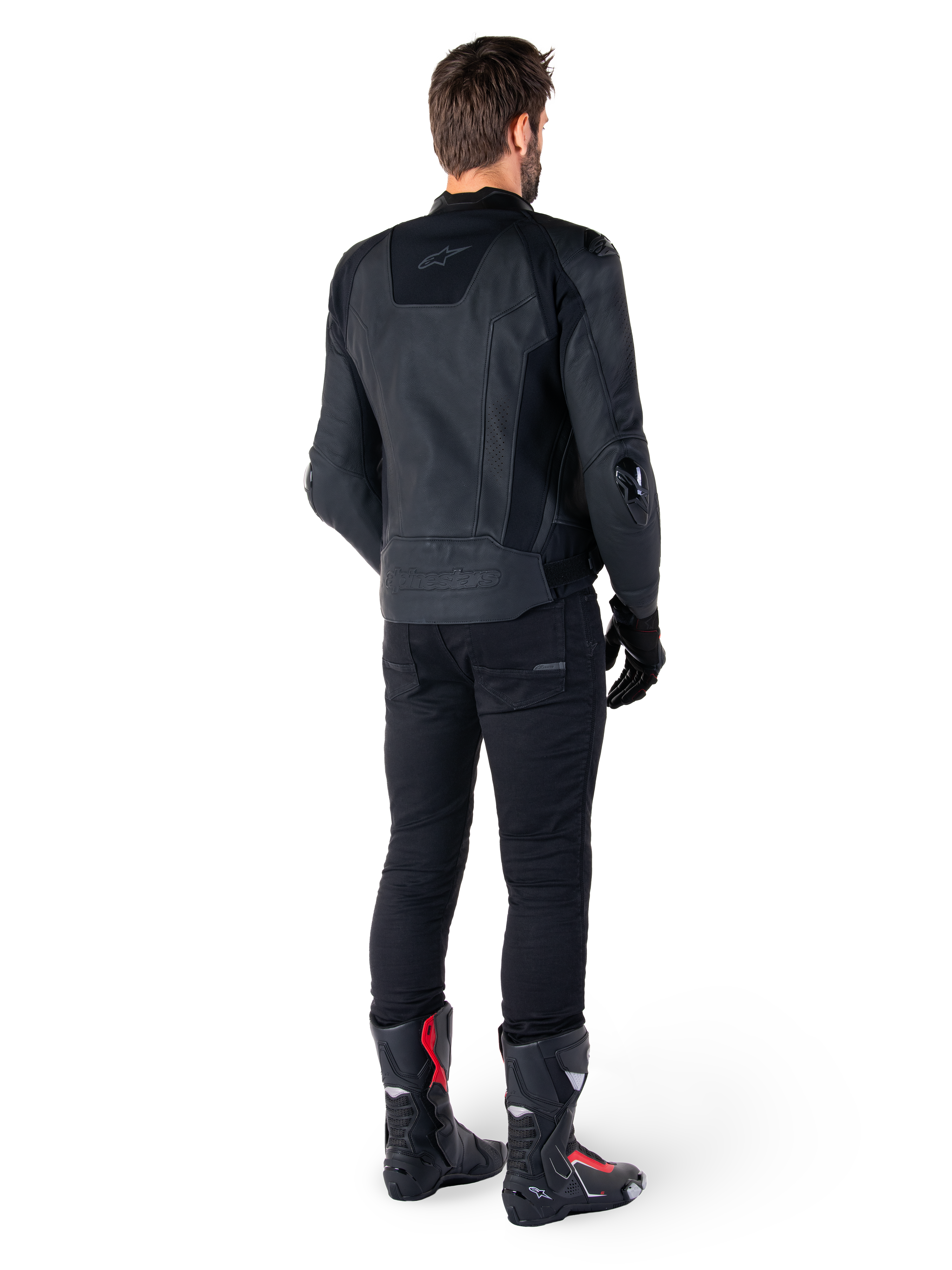 Alpinestars Missile V3 Leather Jacket in nero, vista posteriore su un pilota, indossata con pantaloni neri e stivali da corsa neri e rossi, caratterizzata da una struttura in pelle con branding tono su tono e vestibilità racing performante