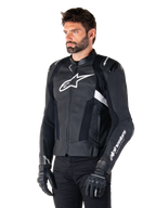 Giacca in pelle Alpinestars Missile V3, nera e bianca, indossata da un uomo con guanti da moto neri, con un prominente logo Alpinestars bianco sul petto, slider esterni sulle spalle e pannelli traforati per un look d'ispirazione racing.