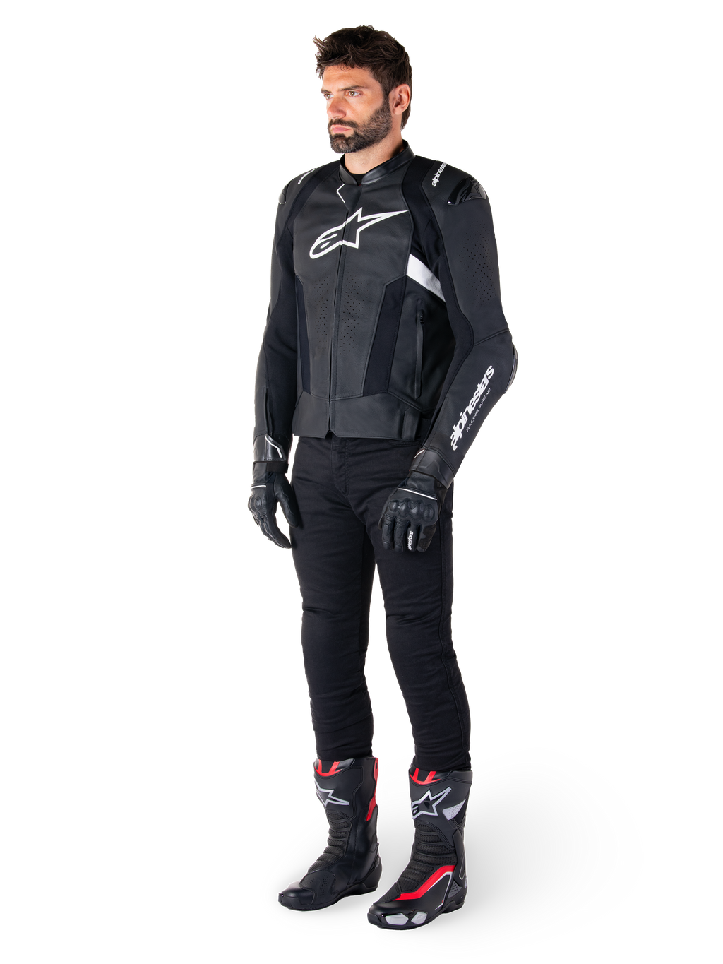 Pilota uomo che indossa la giacca in pelle Alpinestars Missile V3 in nero e bianco, con logo bianco sul petto e pannelli in pelle traforata, abbinata a pantaloni da moto neri, guanti neri e stivali da corsa neri e rossi per un look sportivo completo.
