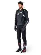 Pilota uomo che indossa la giacca in pelle Alpinestars Missile V3 in nero e bianco, con logo bianco sul petto e pannelli in pelle traforata, abbinata a pantaloni da moto neri, guanti neri e stivali da corsa neri e rossi per un look sportivo completo.