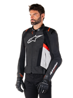 Giacca in pelle Alpinestars Missile V3, nero, bianco e rosso fluo, giacca da moto sportiva da corsa indossata da un modello con guanti e pantaloni neri, caratterizzata da pannelli in pelle traforata e branding Alpinestars in evidenza