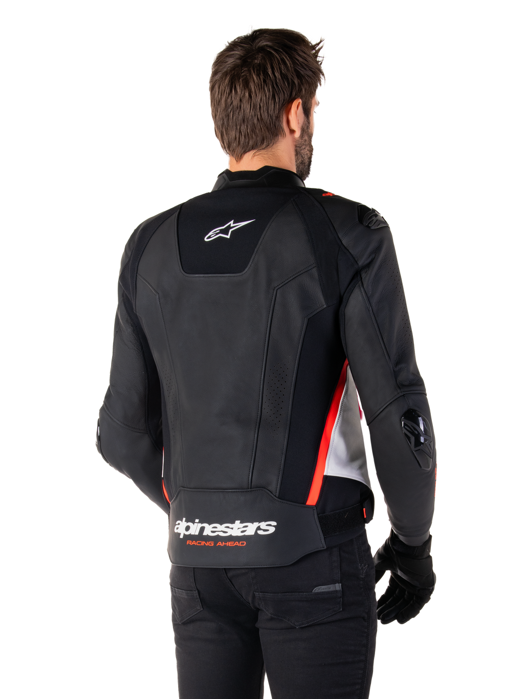 Giacca in pelle Alpinestars Missile V3, vista posteriore su un pilota, nero, bianco e rosso fluo, con branding Alpinestars e scritta 'RACING AHEAD' sulla parte inferiore della schiena, costruzione in pelle premium con pannelli elasticizzati tecnici e slider protettivi in TPU, indossata con guanti e pantaloni neri.