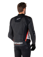 Giacca in pelle Alpinestars Missile V3, vista posteriore su un pilota, nero, bianco e rosso fluo, con branding Alpinestars e scritta 'RACING AHEAD' sulla parte inferiore della schiena, costruzione in pelle premium con pannelli elasticizzati tecnici e slider protettivi in TPU, indossata con guanti e pantaloni neri.