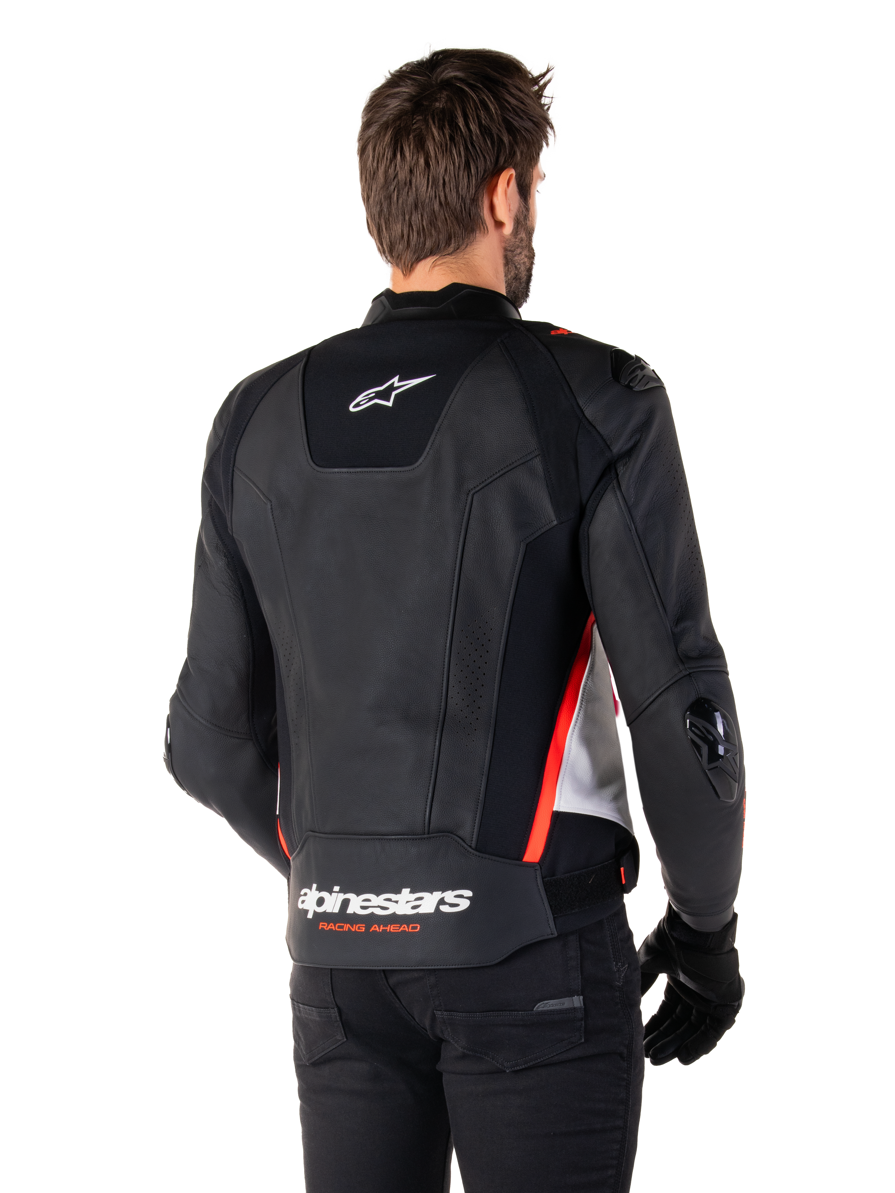 Giacca in pelle Alpinestars Missile V3, vista posteriore su un pilota, nero, bianco e rosso fluo, con branding Alpinestars e scritta 'RACING AHEAD' sulla parte inferiore della schiena, costruzione in pelle premium con pannelli elasticizzati tecnici e slider protettivi in TPU, indossata con guanti e pantaloni neri.