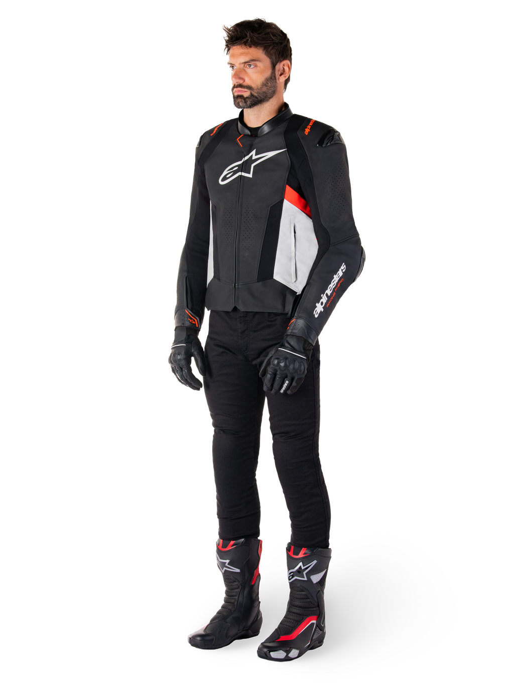 Modello che indossa la giacca in pelle Alpinestars Missile V3 in Nero Bianco e Rosso Fluo, abbinata a pantaloni, guanti e stivali da moto neri, con costruzione in pregiata pelle bovina e logo Alpinestars in evidenza, estetica sportiva professionale da corsa
