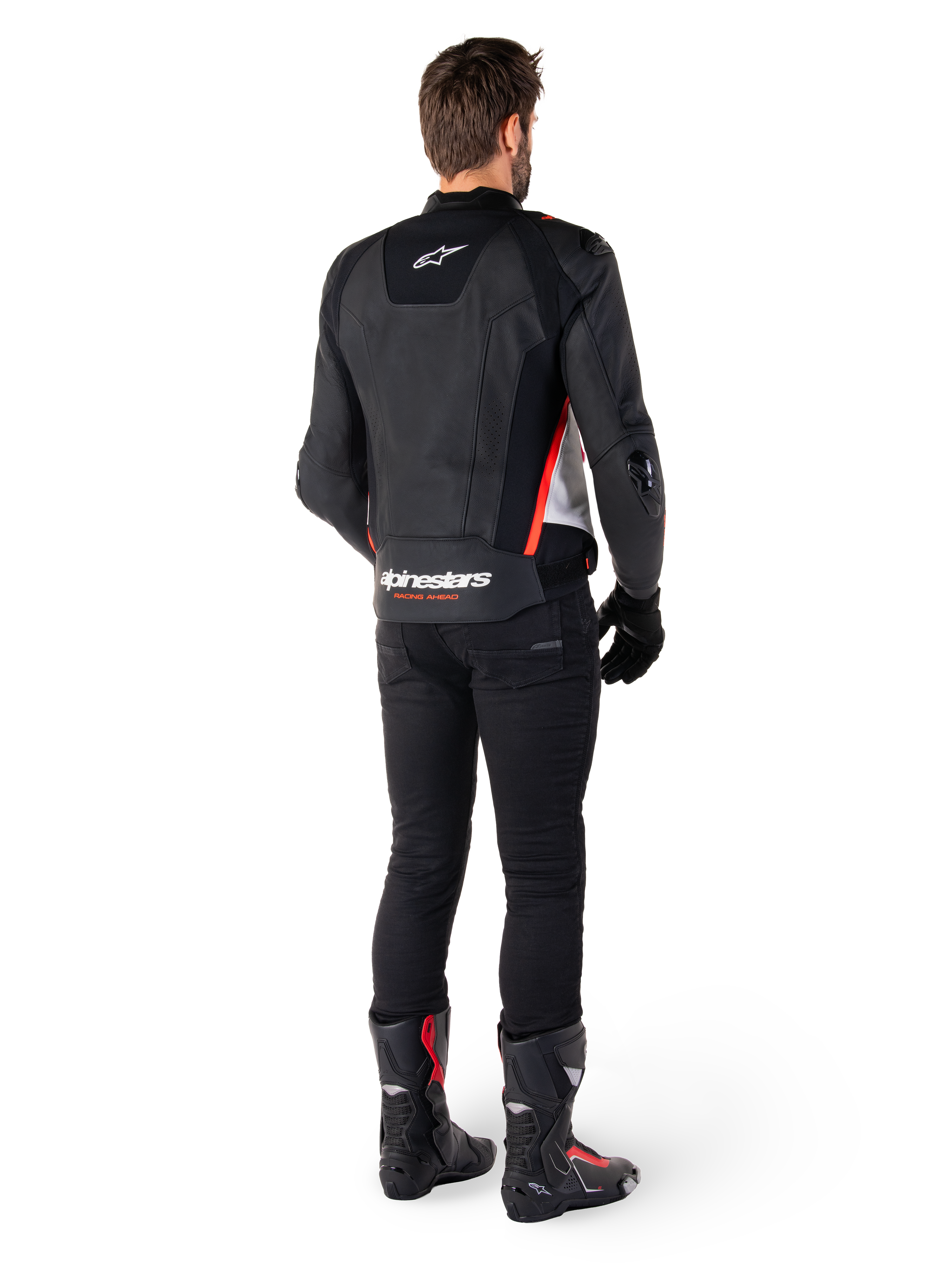 Alpinestars Missile V3 Leather Jacket in Nero Bianco Rosso Fluo, vista posteriore su un pilota uomo, con marchio Alpinestars sulla parte superiore e inferiore della schiena, abbinata a pantaloni neri e stivali da moto, giacca sportiva in pelle d'ispirazione racing.