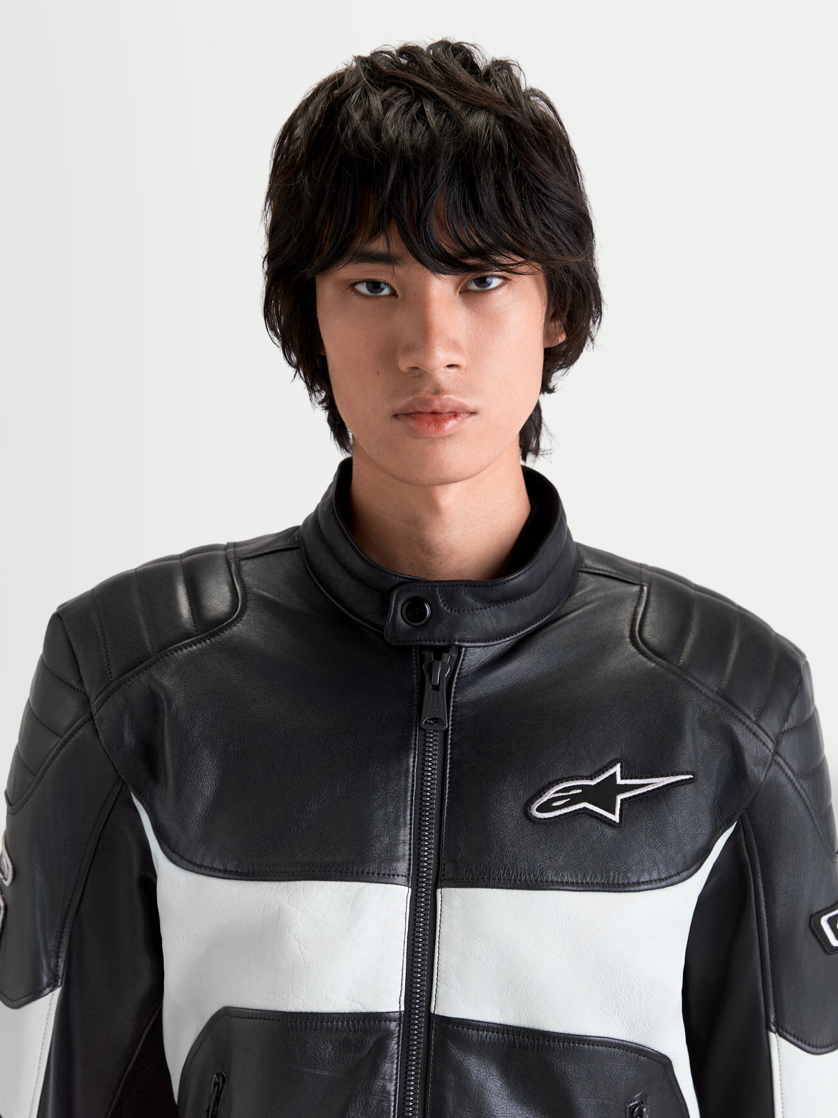 Alpinestars Revern Giacca di pelle, giacca da moto urbana da uomo in nero e grigio metallizzato, vista frontale in primo piano su un modello che mostra la struttura in pelle pieno fiore, collo alla coreana e logo Alpinestars bianco