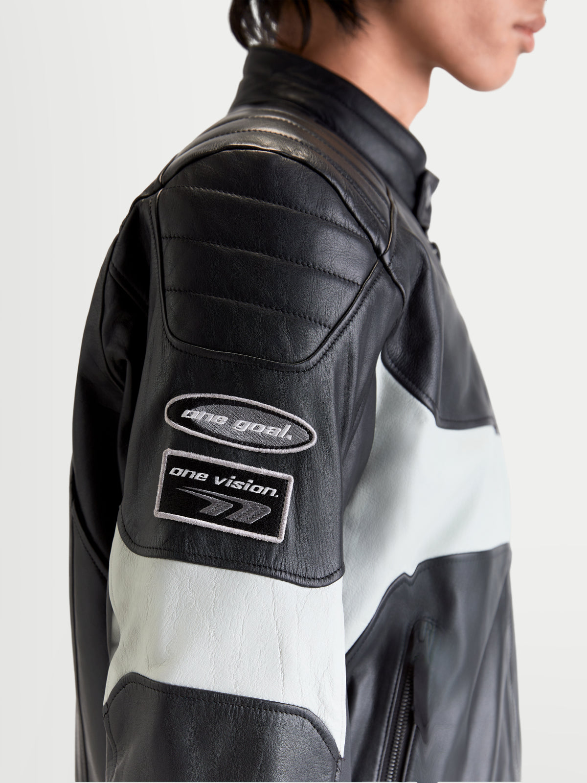 Alpinestars Revern Giacca di pelle, giacca da moto urbana da uomo in pelle nera e grigio metallizzato, primo piano del profilo laterale che mostra le patch con il marchio ispirato alla tradizione sulla manica e la struttura in pelle bovina effetto invecchiato indossata da un modello