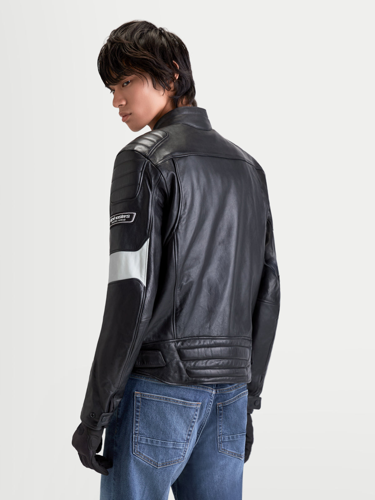 Alpinestars Revern Giacca di pelle, giacca da moto urbana in pelle da uomo in nero e grigio metal, vista posteriore su un modello che indossa jeans, caratterizzata da una struttura in pelle bovina dal look vintage e dettagliheritage