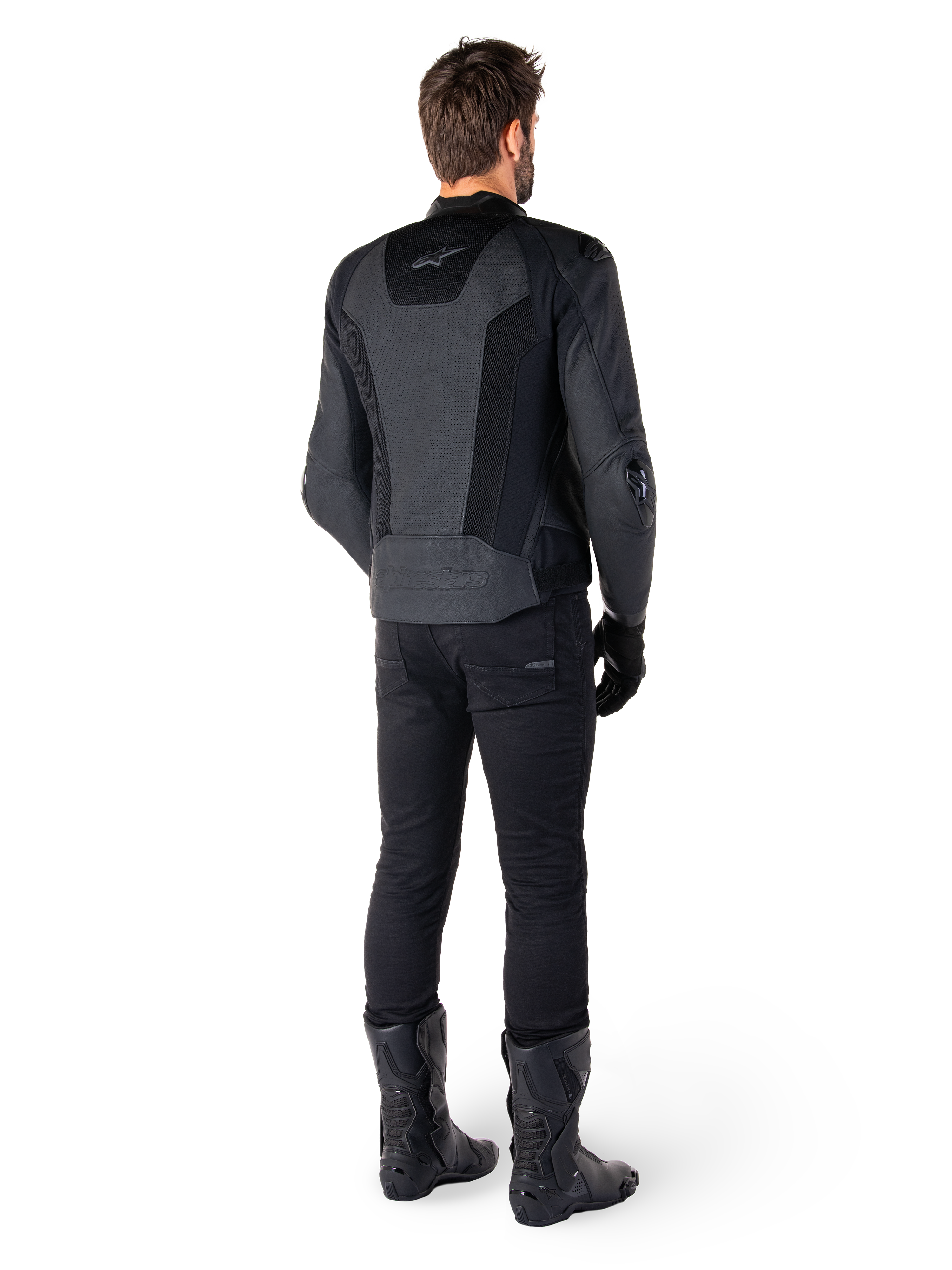 Vista posteriore di un uomo che indossa la giacca in pelle Alpinestars Missile V3 Airflow in nero, dotata di ampi pannelli traforati per la ventilazione, abbinata a pantaloni da moto e stivali neri, che mette in mostra un'estetica racing aerodinamica.
