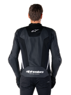 Giacca in pelle Alpinestars Missile V3 Airflow, nero e bianco, vista posteriore indossata da un pilota, con ampi pannelli in pelle traforata, accenti laterali bianchi, logo a stella Alpinestars sulla parte superiore della schiena e marchio 'alpinestars RACING AHEAD' sulla parte inferiore della schiena.