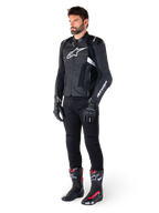 Giacca in pelle Alpinestars Missile V3 Airflow, nero e bianco, indossata da un modello con pantaloni da moto neri, guanti neri e stivali da corsa con accenti rossi e bianchi, con pelle traforata e loghi bianchi, abbigliamento tecnico da moto racing