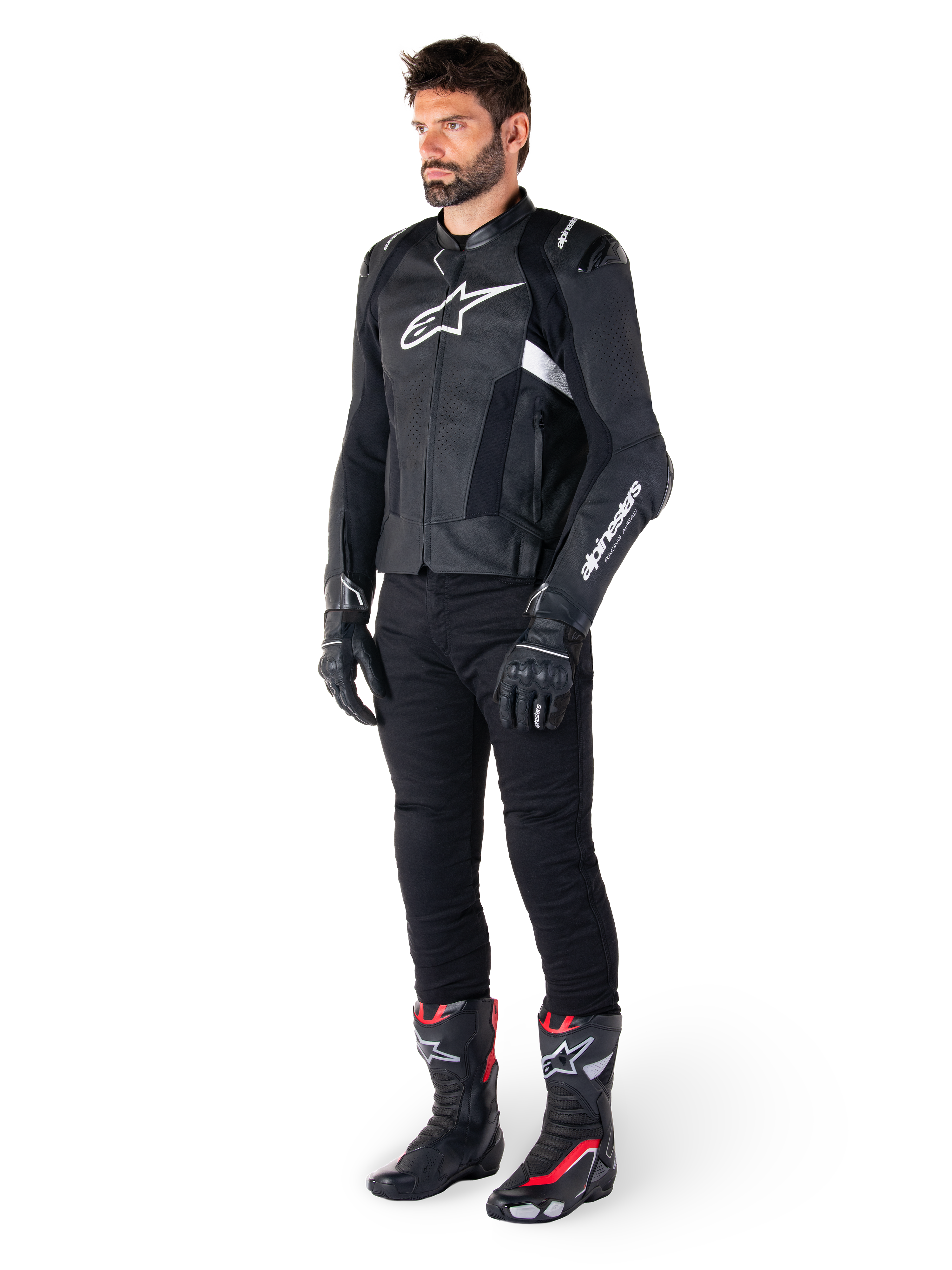 Giacca in pelle Alpinestars Missile V3 Airflow, nero e bianco, indossata da un modello con pantaloni da moto neri, guanti neri e stivali da corsa con accenti rossi e bianchi, con pelle traforata e loghi bianchi, abbigliamento tecnico da moto racing