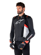Alpinestars Missile V3 Airflow Leather Jacket, giacca da moto sportiva racing, nero bianco e rosso fluo, indossata da un modello con guanti coordinati, caratterizzata da pannelli in pelle traforata, grande logo bianco sul petto e slider sulle spalle neri.