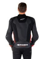 Vista posteriore di una persona che indossa la giacca in pelle Alpinestars Missile V3 Airflow in Nero Bianco Rosso Fluo, caratterizzata da ampi pannelli in pelle traforata per la ventilazione, un piccolo logo Alpinestars sulla parte superiore della schiena e il marchio 'alpinestars RACING AHEAD' sulla parte inferiore della vita.