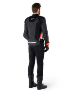 Pilota visto di spalle che indossa la giacca in pelle Alpinestars Missile V3 Airflow in Nero Bianco Rosso Fluo, abbinata a pantaloni neri e stivali neri, con ampie zone in pelle traforata per la ventilazione, protezioni DFS sulle spalle e logo Alpinestars in evidenza sulla parte bassa della schiena.