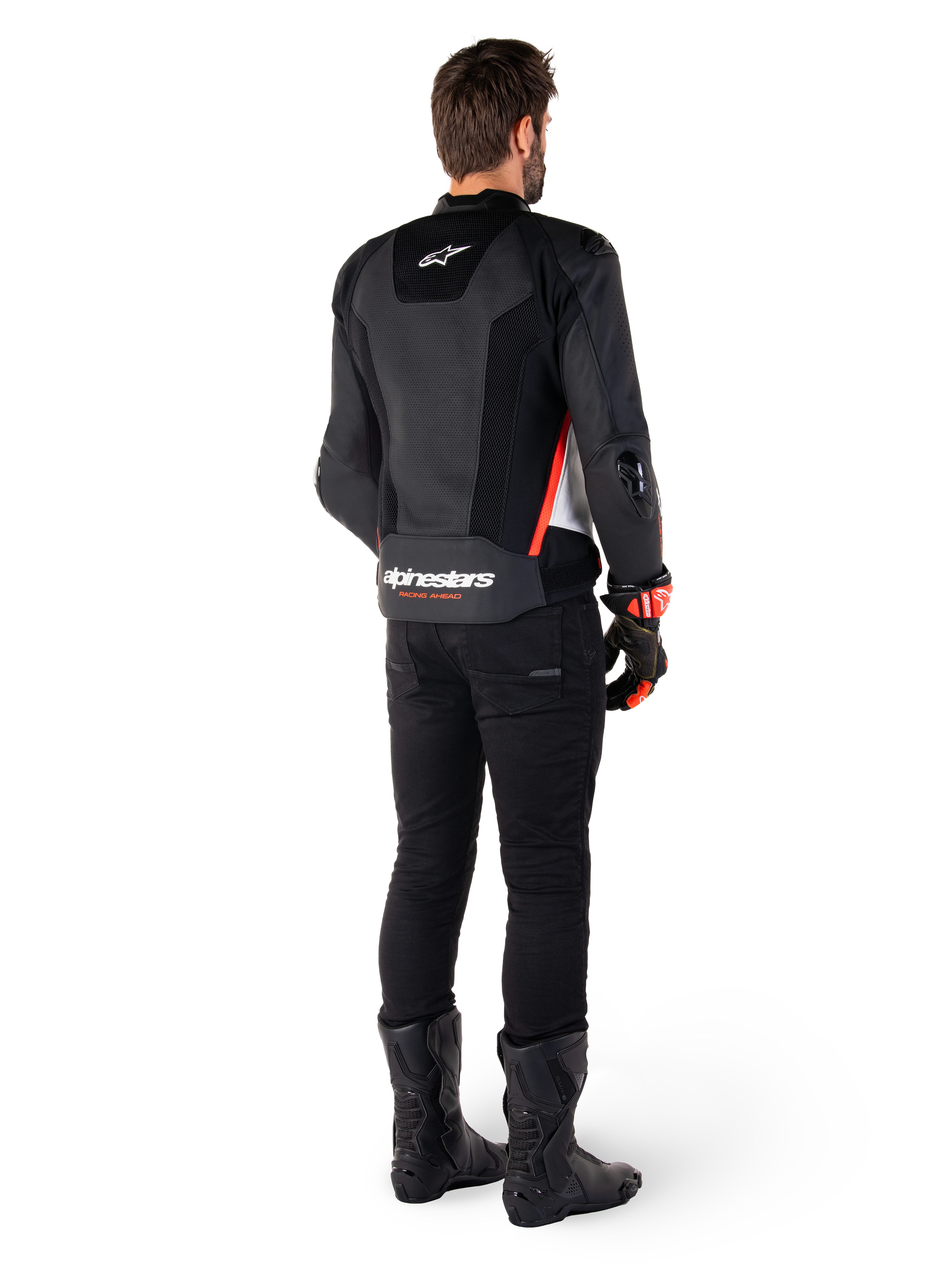 Pilota visto di spalle che indossa la giacca in pelle Alpinestars Missile V3 Airflow in Nero Bianco Rosso Fluo, abbinata a pantaloni neri e stivali neri, con ampie zone in pelle traforata per la ventilazione, protezioni DFS sulle spalle e logo Alpinestars in evidenza sulla parte bassa della schiena.