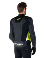Alpinestars Missile V3 Airflow Leather Jacket, vista posteriore su un modello, nero con accenti giallo fluorescente e bianco, ampi pannelli in pelle traforata e mesh sulla schiena, logo a stella giallo e scritta 'RACING AHEAD' bianca, abbinata a guanti e pantaloni neri.