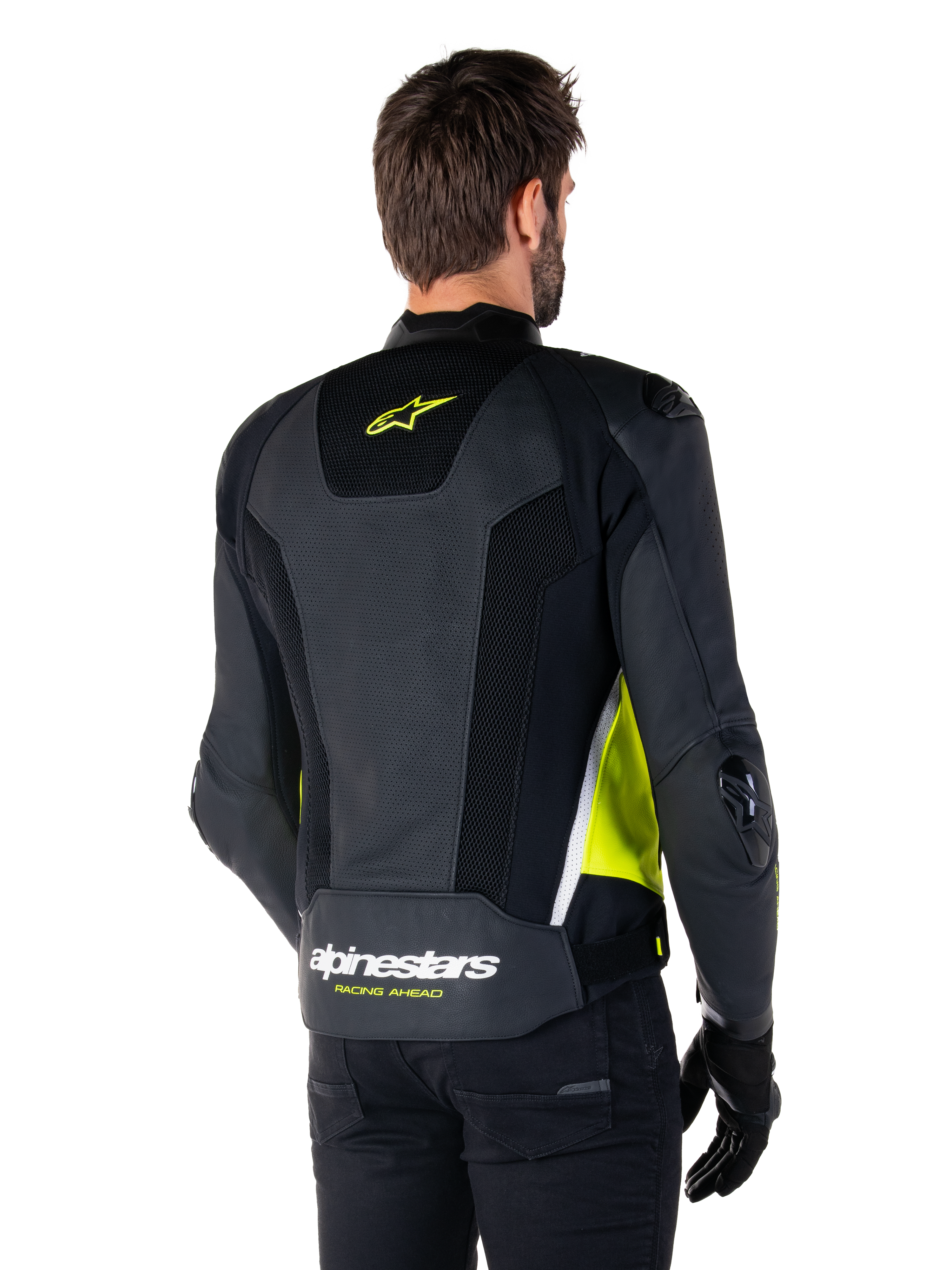 Alpinestars Missile V3 Airflow Leather Jacket, vista posteriore su un modello, nero con accenti giallo fluorescente e bianco, ampi pannelli in pelle traforata e mesh sulla schiena, logo a stella giallo e scritta 'RACING AHEAD' bianca, abbinata a guanti e pantaloni neri.