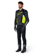 Modello uomo che indossa la giacca in pelle Alpinestars Missile V3 Airflow in nero, giallo fluo e bianco, abbinata a guanti, pantaloni e stivali da moto neri, che mette in risalto il design in pelle traforata e l'estetica ispirata alle corse.