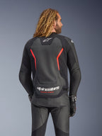 Giacca in pelle Alpinestars GP Force V2, nero e rosso fluo, vista posteriore su un modello, con logo Alpinestars bianco e scritta 'RACING AHEAD', abbinata a pantaloni e guanti da moto in pelle nera.