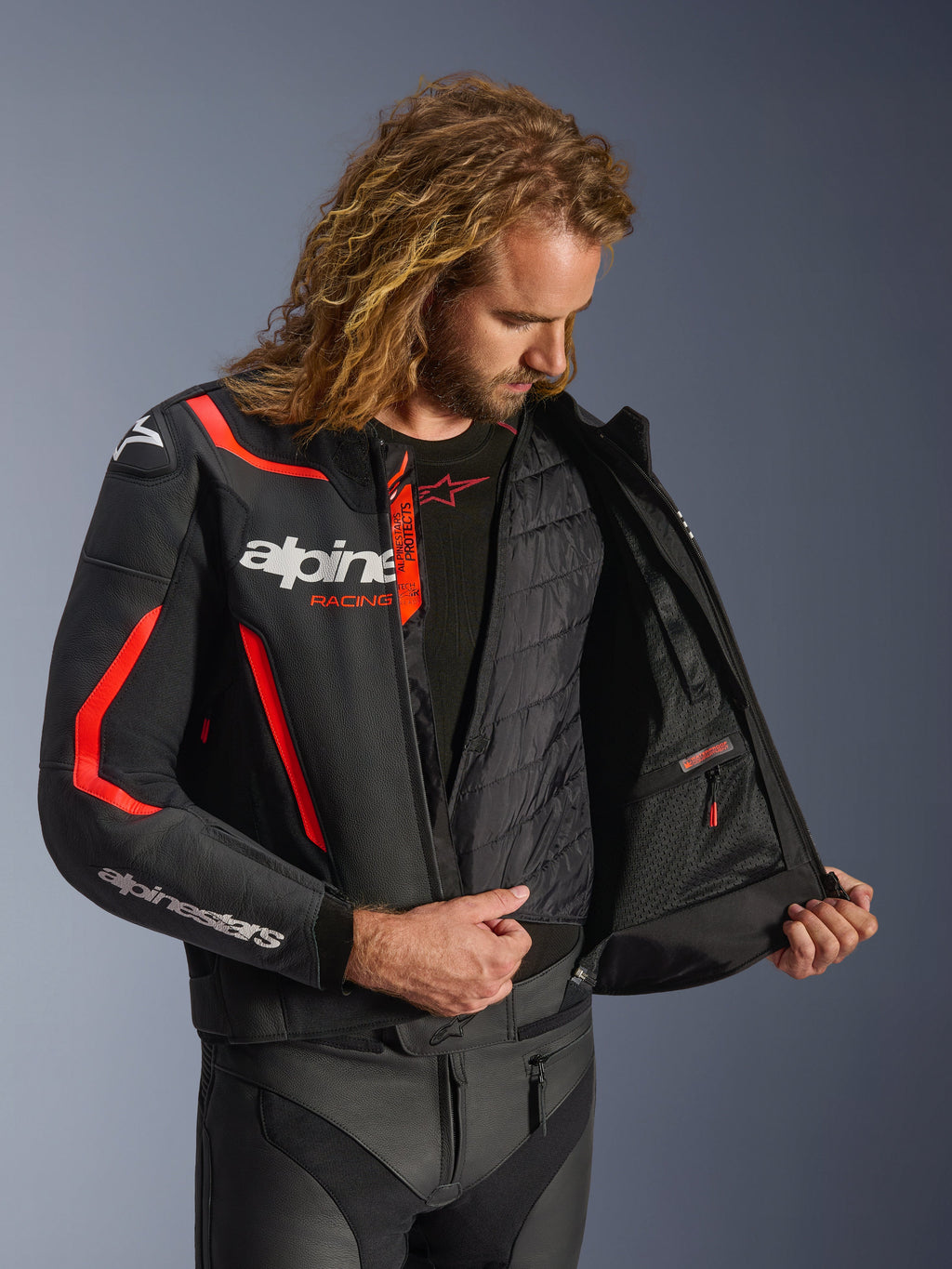 Giacca in pelle Alpinestars GP Force V2 in nero e rosso fluo, vista interna dettagliata su modello che mostra il gilet termico rimovibile e la tasca interna impermeabile, costruzione in pelle premium per la protezione nella guida sportiva.