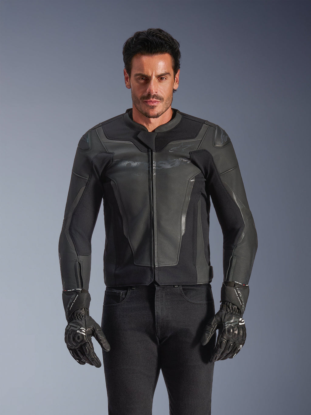 Giacca in pelle Alpinestars GP Force V2, nero e grigio scuro, giacca da moto racing, uomo che indossa un design in pelle aderente con zip frontale, abbinata a guanti neri testurizzati, abbigliamento protettivo moderno, costruzione in pelle premium