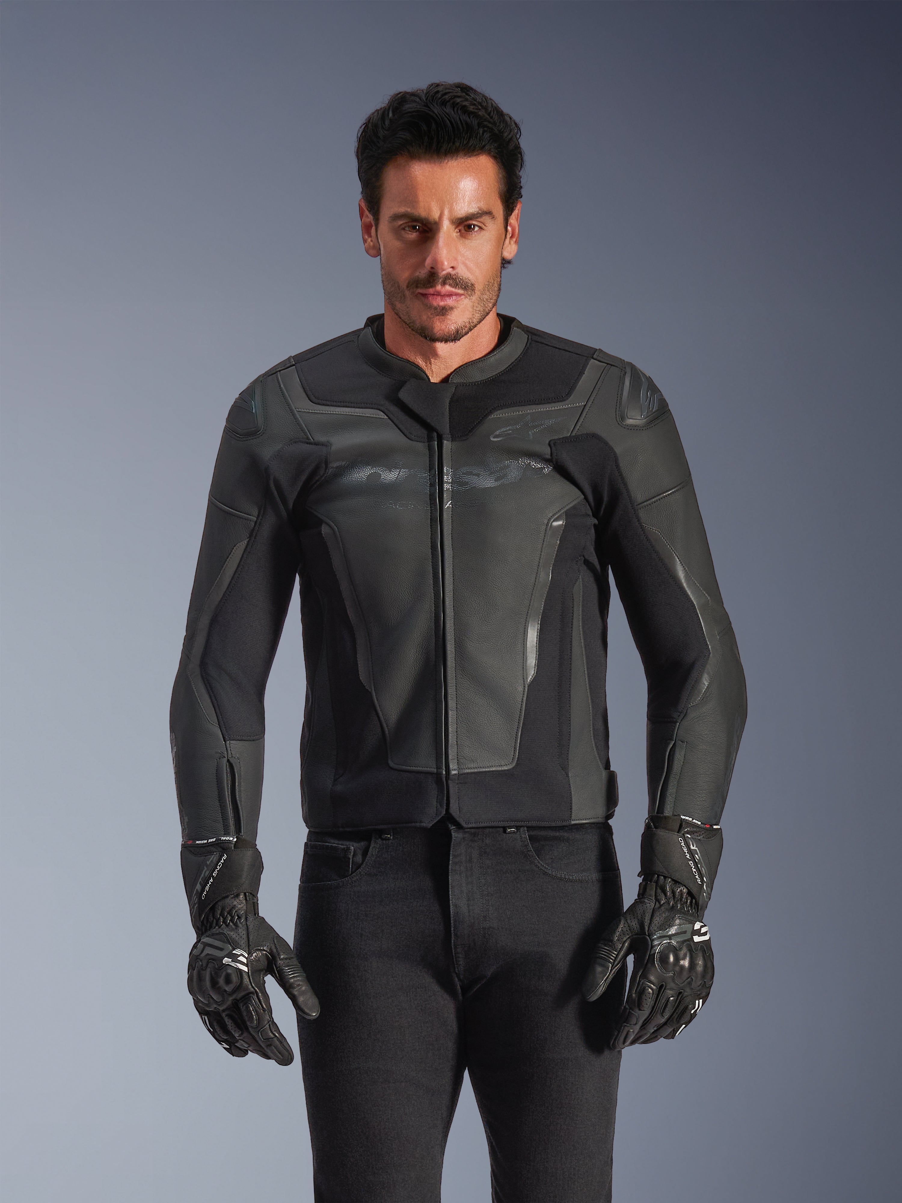 Giacca in pelle Alpinestars GP Force V2, nero e grigio scuro, giacca da moto racing, uomo che indossa un design in pelle aderente con zip frontale, abbinata a guanti neri testurizzati, abbigliamento protettivo moderno, costruzione in pelle premium