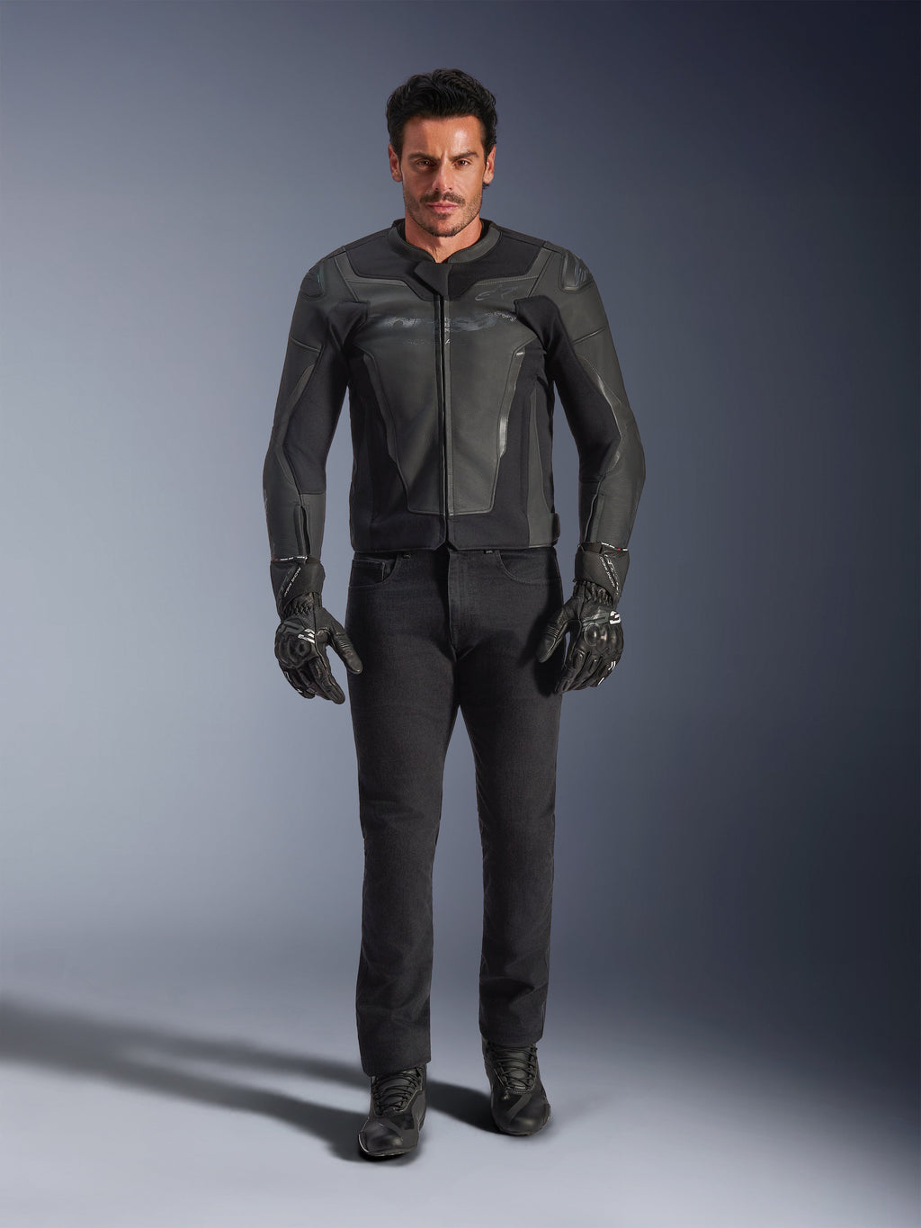 Giacca in pelle Alpinestars GP Force V2 nera, indossata da un motociclista con pantaloni, guanti e stivali da moto neri, costruzione in pelle dal design sportivo con slider sulle spalle e protezioni integrate.