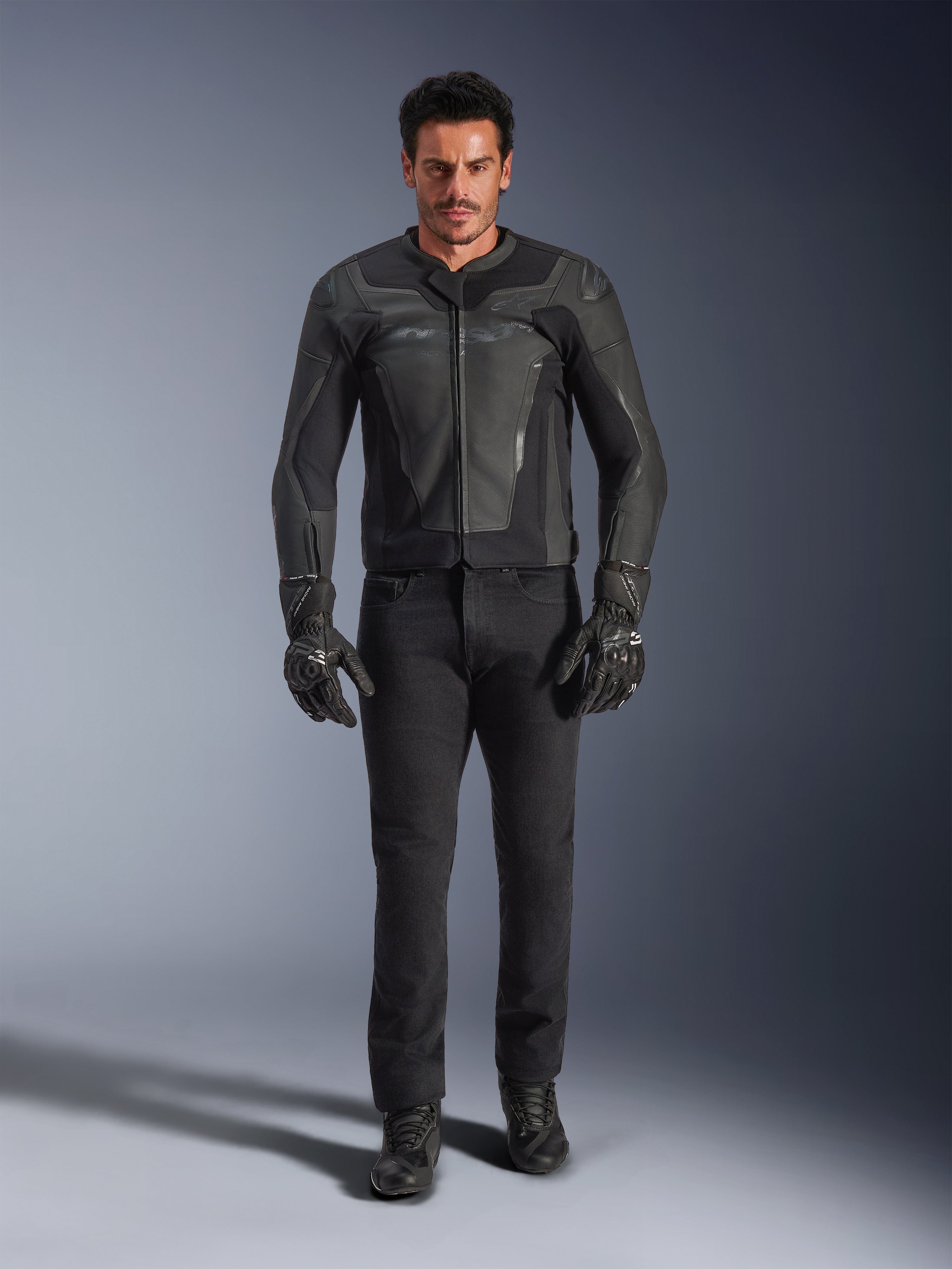 Giacca in pelle Alpinestars GP Force V2 nera, indossata da un motociclista con pantaloni, guanti e stivali da moto neri, costruzione in pelle dal design sportivo con slider sulle spalle e protezioni integrate.