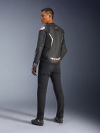 Giacca in pelle Alpinestars GP Force V2, nero e bianco, vista posteriore che mostra la costruzione in pelle con accenti bianchi e loghi rossi, indossata con pantaloni neri e guanti racing, con evidente marchio Alpinestars sulla parte bassa della schiena, abbigliamento da moto sportivo