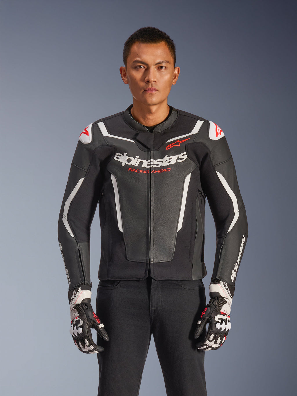 Giacca in pelle Alpinestars GP Force V2, nero e bianco con accenti rossi, giacca da moto racing, costruzione in pelle premium con protezioni, marchio Racing Ahead, indossata con guanti coordinati