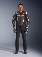 Modello che indossa la giacca in pelle Alpinestars GP Force V2 in nero e bianco, abbinata a pantaloni da moto neri e guanti bianchi e neri, con marchio Alpinestars in evidenza e accenti rossi sulle spalle, abbigliamento professionale per la guida sportiva in moto
