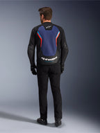 Giacca in pelle Alpinestars GP Force V2, giacca da moto sportiva, Nero Blu Rosso Fluo, vista posteriore su un modello, caratterizzata da un ampio pannello posteriore blu con accenti rossi e azzurri e marchio Alpinestars bianco sulla parte inferiore della schiena, abbinata a pantaloni da moto e guanti neri.