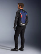 Vista posteriore a tre quarti di un modello che indossa la giacca in pelle Alpinestars GP Force V2 in Black Blue Red Fluo, che mette in risalto il pannello posteriore blu con accenti rosso fluorescente e logo bianco, abbinata a pantaloni neri e guanti da moto.