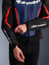 Giacca in pelle Alpinestars GP Force V2 in nero, blu e rosso fluo, vista ravvicinata di una persona che regola la cerniera del polsino, con loghi Alpinestars bianchi su avambraccio e petto, costruzione in pelle bovina testurizzata per guida sportiva