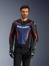 Giacca in pelle Alpinestars GP Force V2, nero, blu e rosso fluo, indossata da un modello con guanti e pantaloni neri, caratterizzata da un pannello blu sul petto con scritta 'Alpinestars Racing Ahead', dettagli rossi e scudi esterni sulle spalle, abbigliamento protettivo da moto sportiva