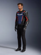 Modello che indossa la giacca in pelle Alpinestars GP Force V2 in Black Blue Red Fluo, abbinata a pantaloni tecnici neri, guanti e stivali neri, abbigliamento professionale da motociclismo per guida sportiva