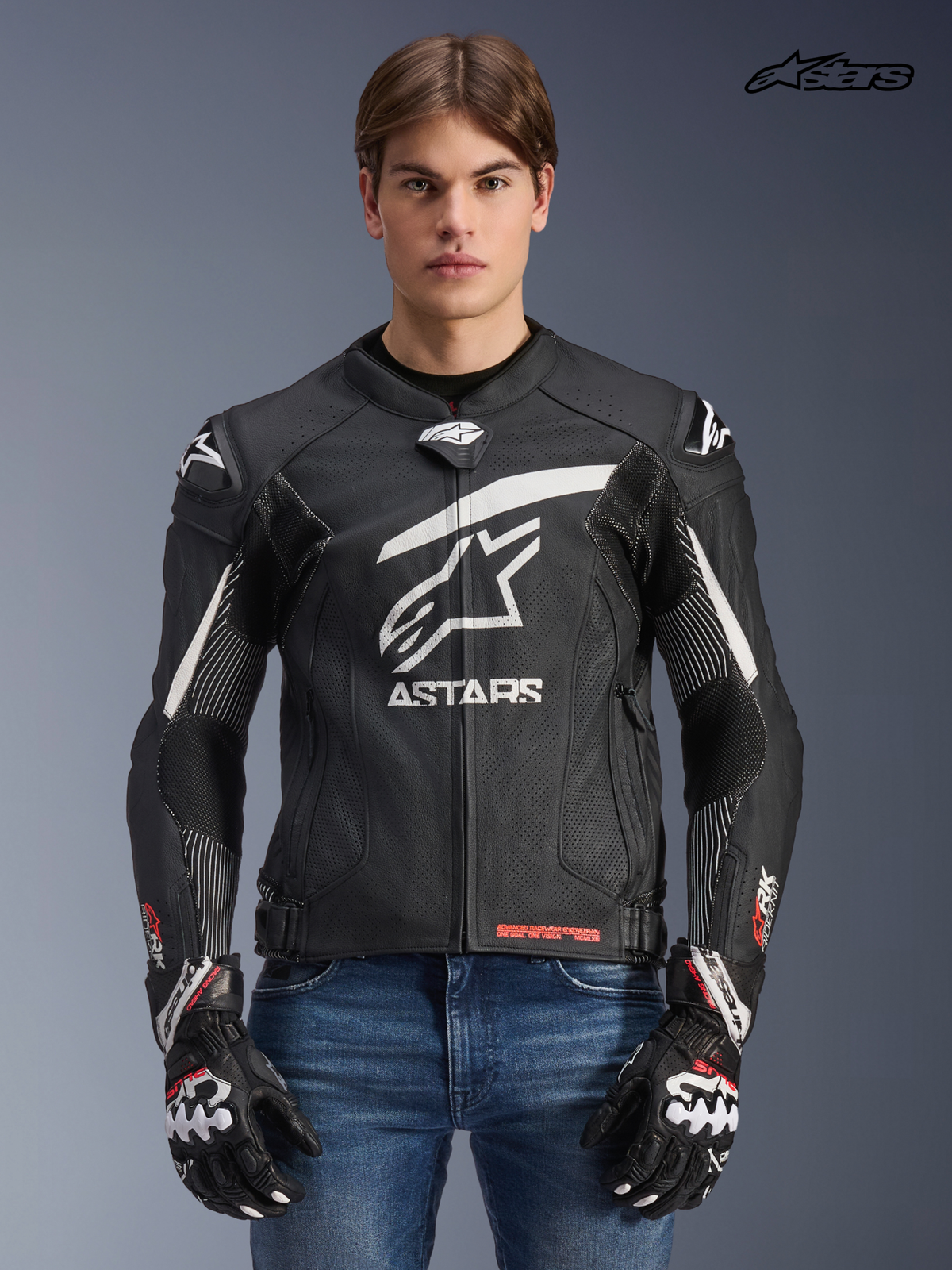 Alpinestars Giacca In Pelle GP Plus R V4 Rideknit, giacca da moto sportiva da uomo in nero e bianco, vista frontale su un modello con guanti coordinati e jeans, protezione derivata dalla corsa e pannelli elasticizzati ingegnerizzati