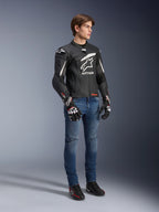 Giacca in pelle Alpinestars GP Plus R V4 Rideknit, nero e bianco, giacca da moto in pelle indossata da un modello con jeans blu e guanti neri, caratterizzata da un prominente logo Astars bianco sul petto, pannelli traforati e dettagli bianchi sulle spalle.